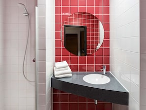 Un baño moderno con un espejo redondo, un lavamanos blanco y un cabezal de ducha.