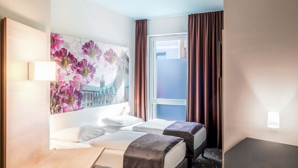 A hotel room with two beds, a desk, and a large floral artwork on the wall. - B&B Hotel Hildesheim (Hildesheim)