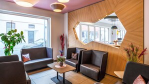 A modern waiting area with leather seating, a central coffee table, and a large window offering a view of the street. - B&B Hotel Hildesheim (Hildesheim)