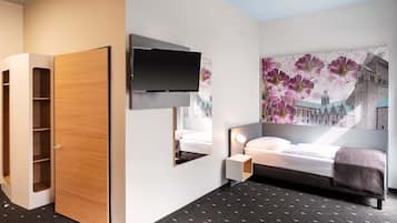 A modern hotel room with a bed, a TV mounted on the wall, a wooden wardrobe, and a large floral artwork on the wall.