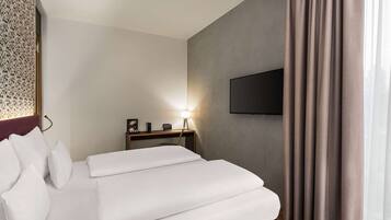 Habitación de hotel con cama, escritorio con lámpara, televisor de pantalla plana y cortina.