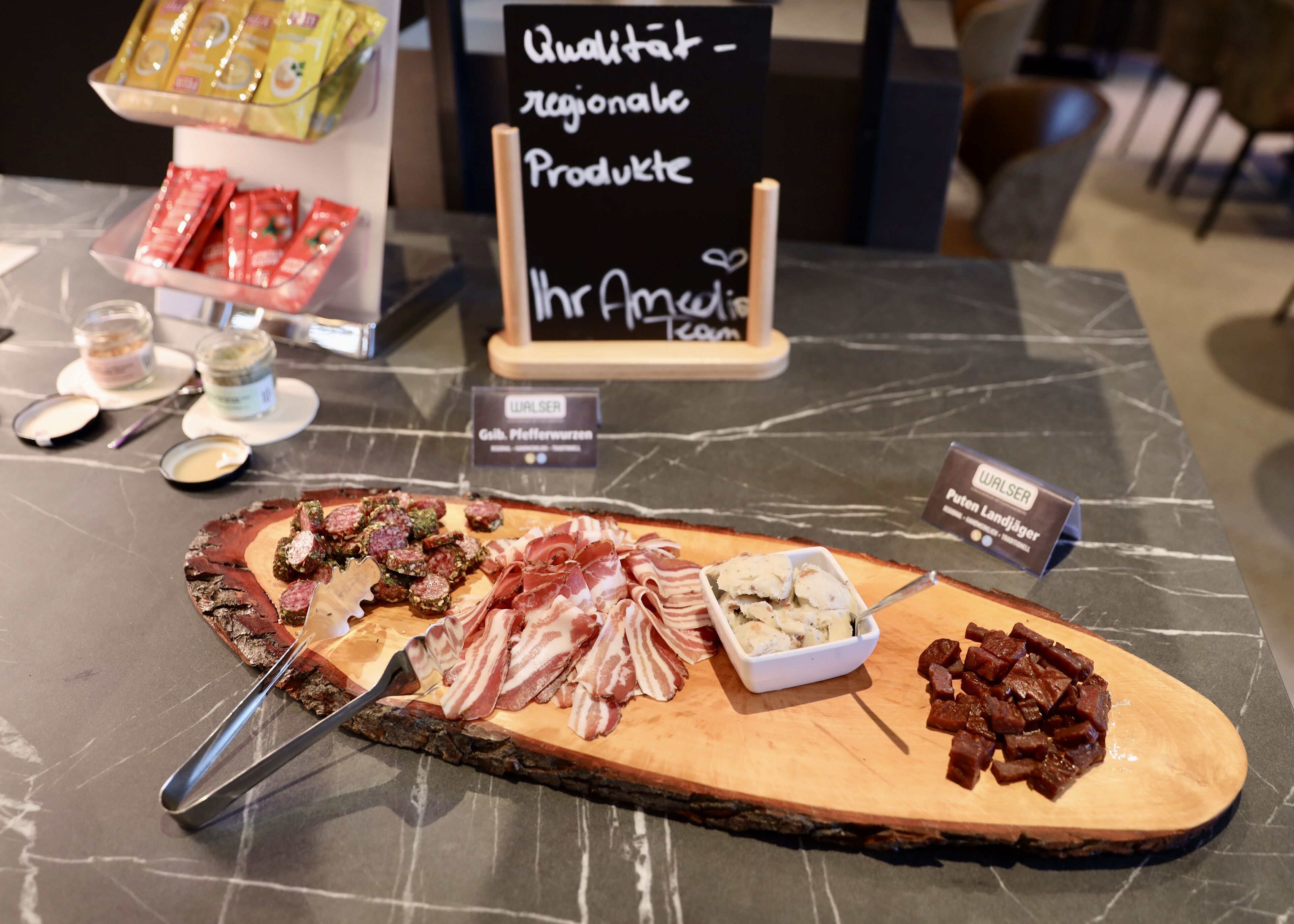 A charcuterie board with various meats and cheeses on a wooden board, accompanied by small bowls of dips and condiments, set on a marble table.