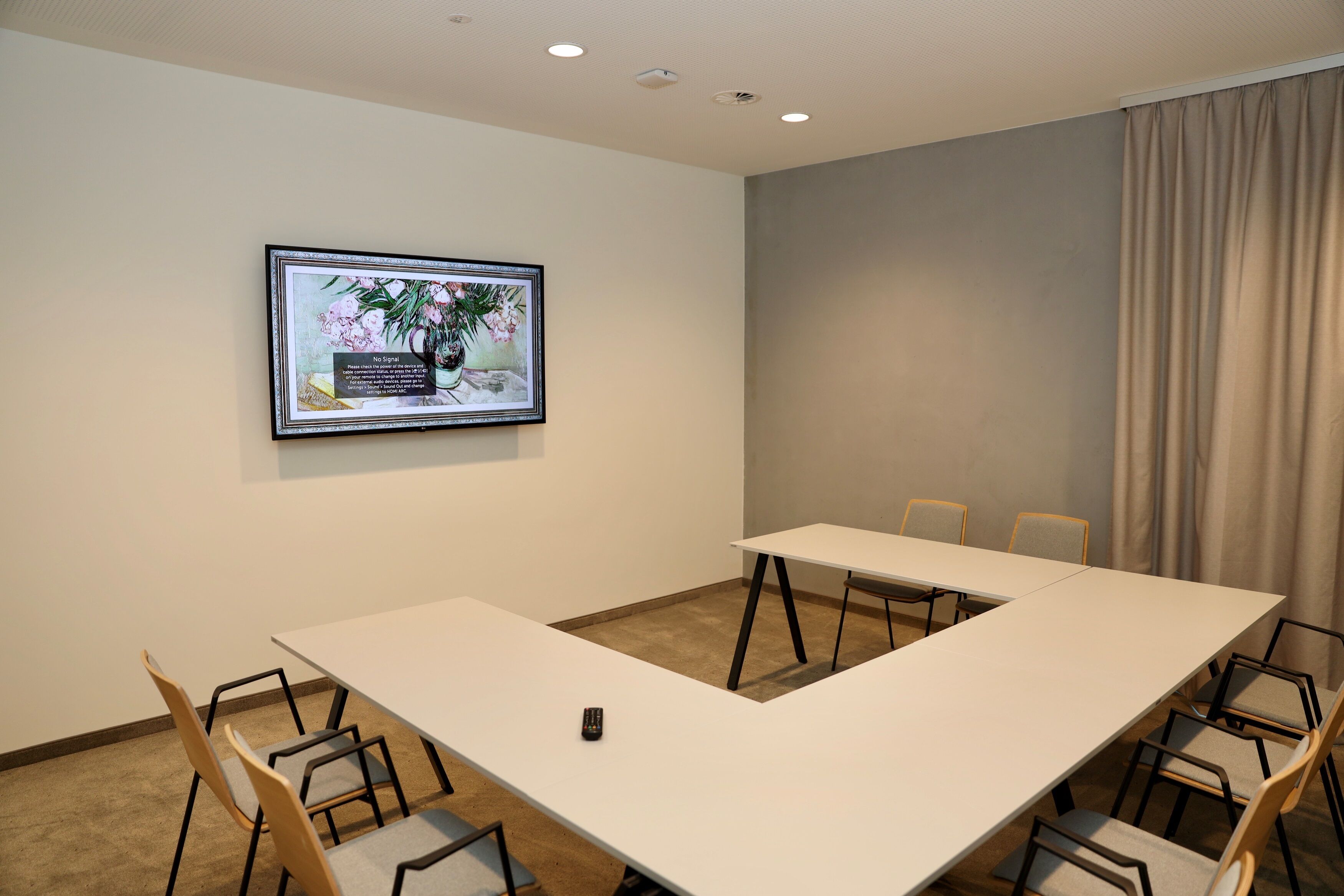 Une salle de conférence avec une longue table, des chaises, un tableau encadré au mur et un rideau à la fenêtre.