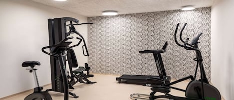 A fitness room with exercise equipment including a stationary bike, elliptical, and treadmill.