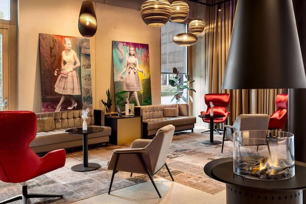 A modern lounge area with a sofa, red chairs, a fireplace, and artwork on the walls. - Radisson Hotel Lustenau (Lustenau)