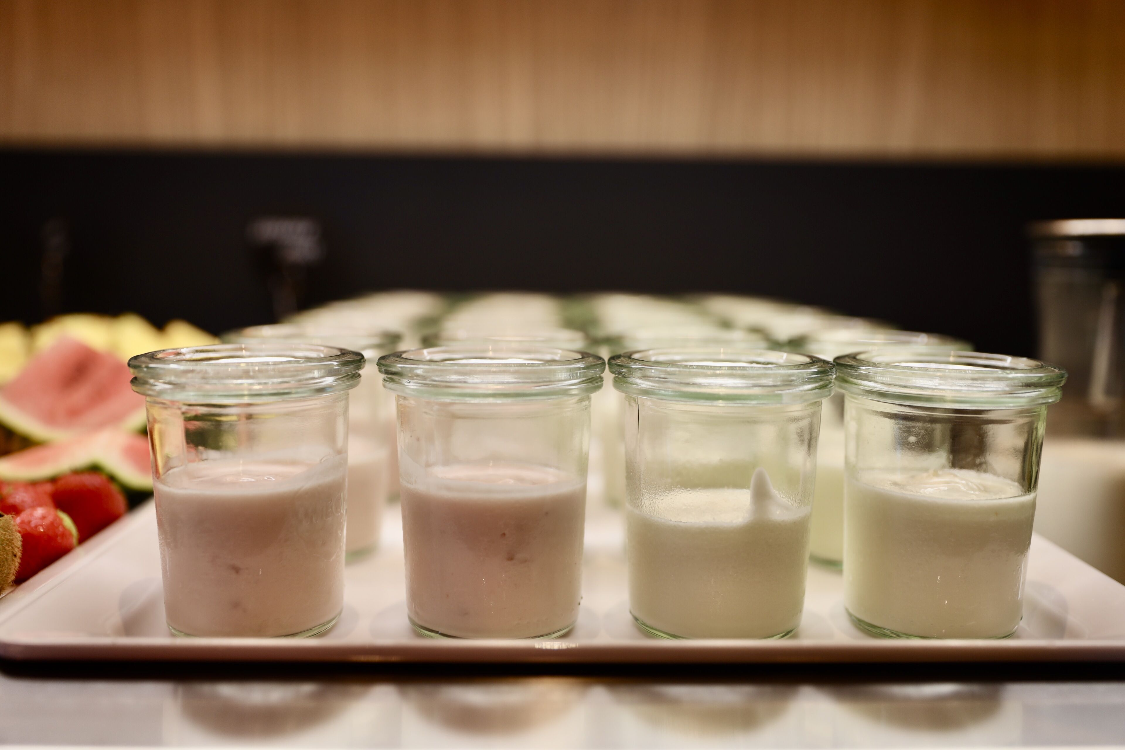 Un plateau sur lequel sont disposés quatre pots en verre contenant une substance crémeuse blanche, qui pourrait être du yaourt ou un produit laitier similaire, le tout présenté sur une assiette blanche.