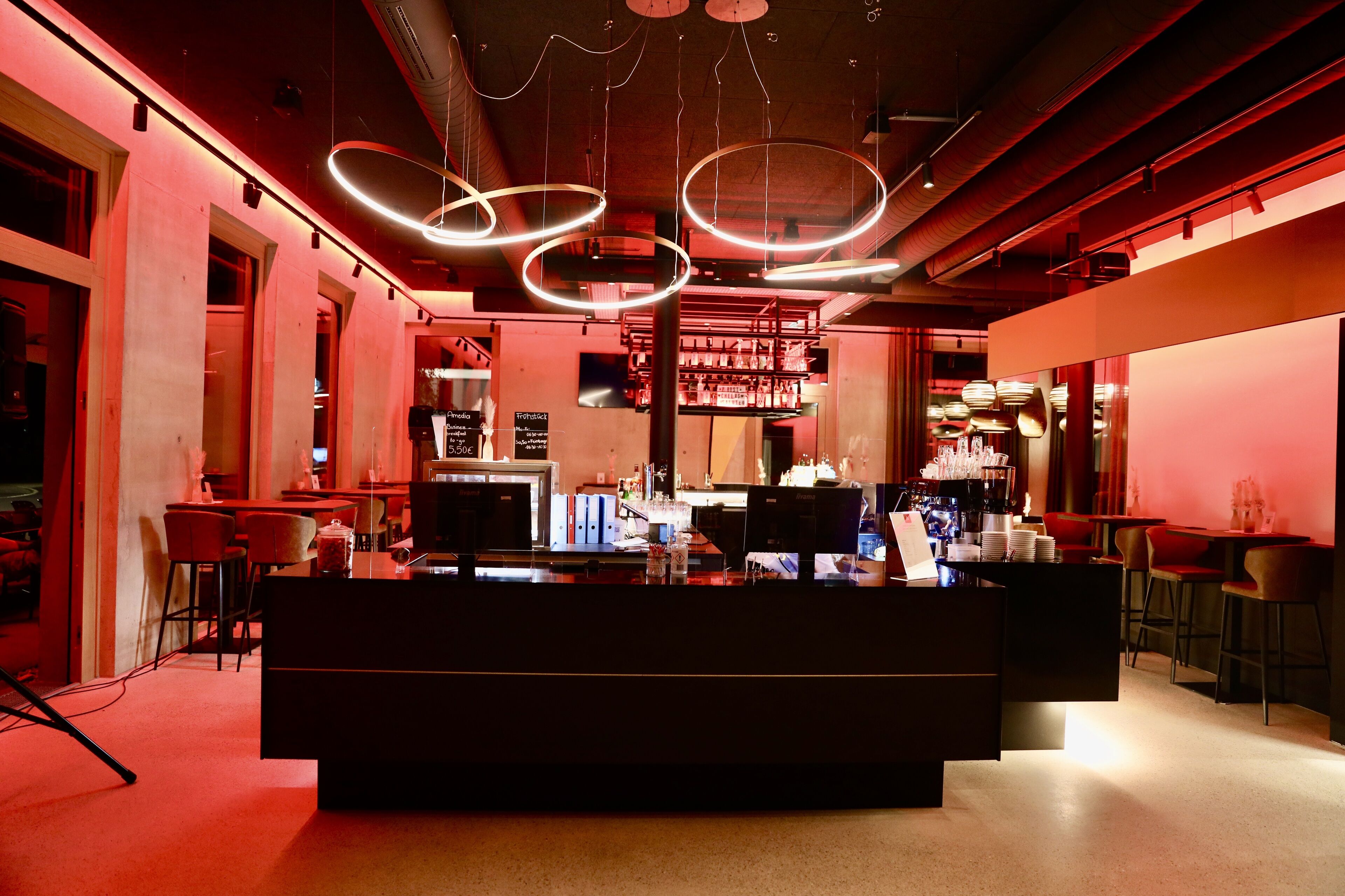 Un área de bar moderna con una barra central, taburetes y lámparas circulares colgantes.