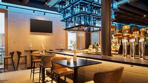 A modern bar area with multiple seating options, a high shelf with bottles, and a large screen on the wall. - Radisson Hotel Lustenau (Lustenau)