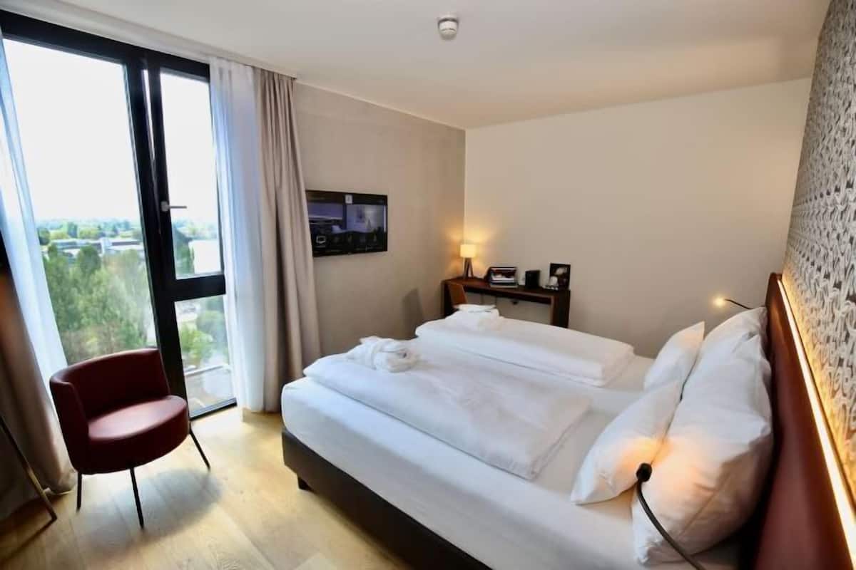 A hotel room with a large bed, a TV, a chair, and a view of the outdoors.