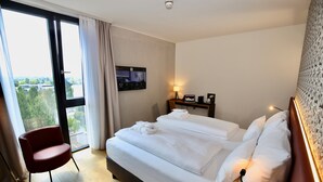 A hotel room with a bed, a chair, a TV, and a window with curtains. - Radisson Hotel Lustenau (Lustenau)