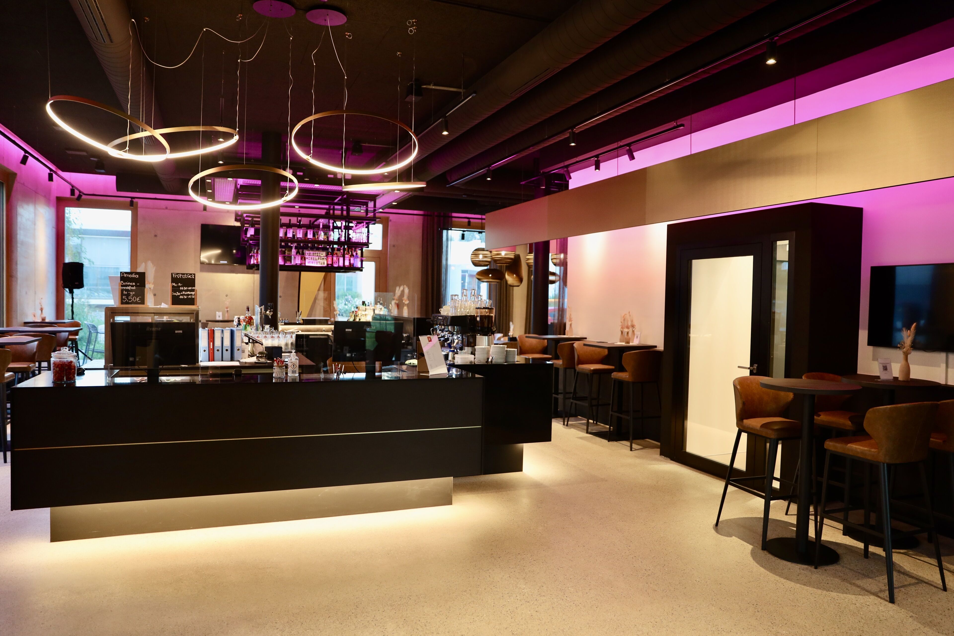 A modern bar area with a central counter, bar stools, and a seating area with tables and chairs.