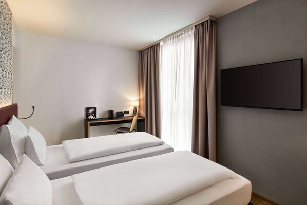 Una habitación de hotel con una cama, un escritorio, una silla y un televisor en la pared.