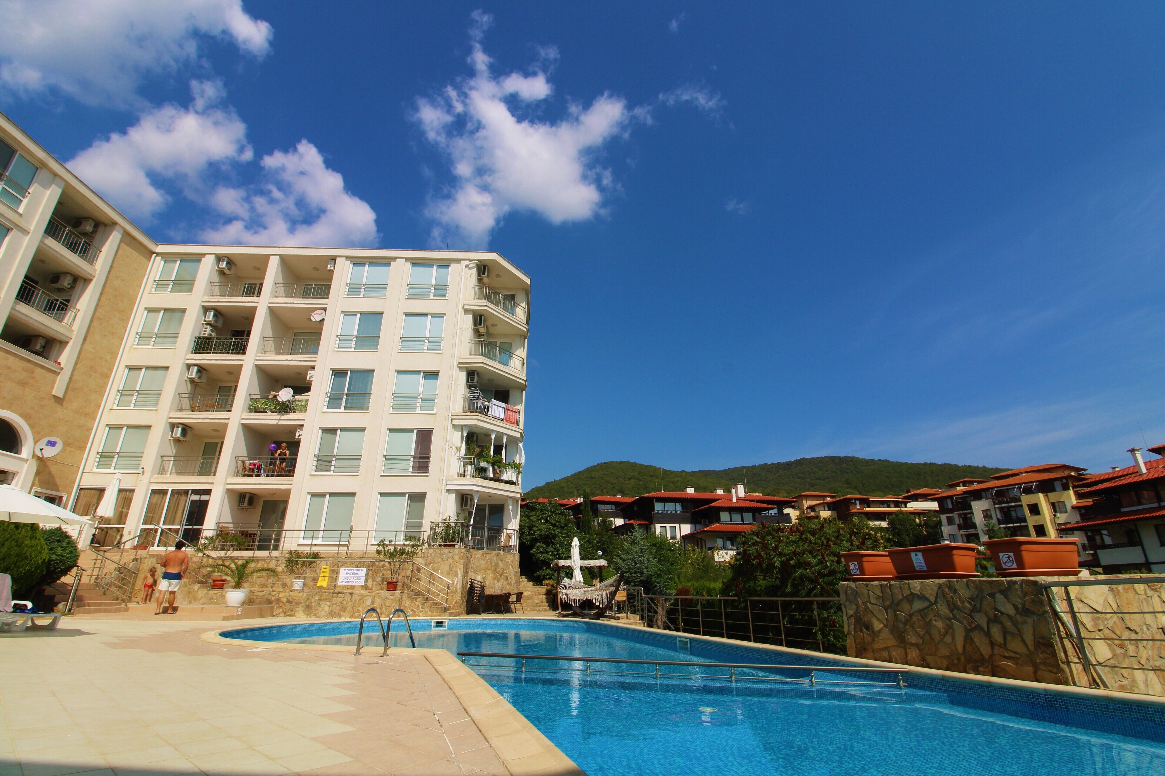 A hotel with a swimming pool, multiple balconies, and a view of the surrounding landscape.