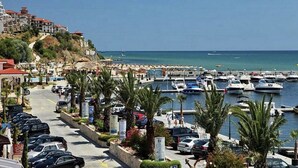 A coastal marina with parked cars and boats, a clear sky, and buildings on a hillside. - Menada Galateya Apartments (Sveti Vlas)