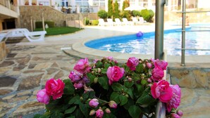 A pool area with a stone pathway, lounge chairs, and a building with arched windows in the background. - Menada Galateya Apartments (Sveti Vlas)