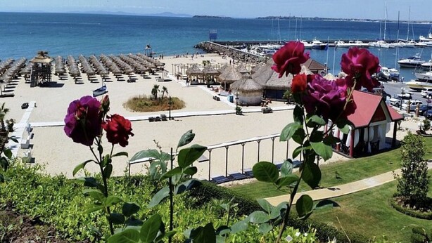 A coastal view with a marina, beach umbrellas, and a small building with a red roof. - Menada Galateya Apartments (Sveti Vlas)
