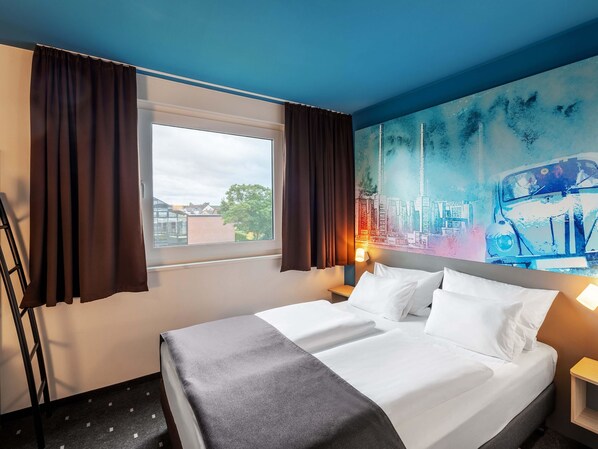 Una habitación de hotel con una cama, una ventana con cortinas, un cuadro en la pared y una mesita de noche con una lámpara.