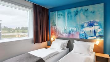 A hotel room with two beds, a large window, and a cityscape painting on the wall.