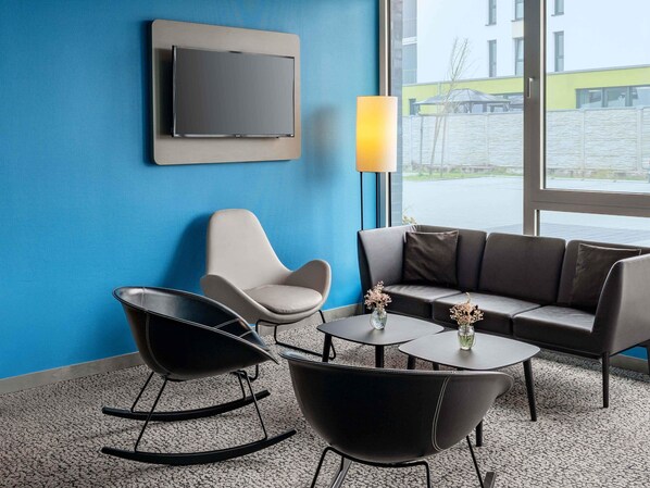 Un área de descanso moderna con una pared azul, un televisor de pantalla plana, un sofá, dos sillones mecedores y una mesa de centro con un jarrón.