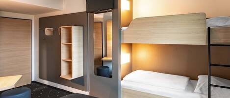 A modern hotel room with a bunk bed, a desk with a chair, a small seating area, and a large mirror.