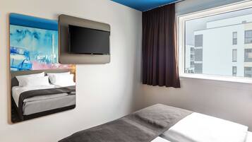 A hotel room with a bed, a flat-screen TV mounted on the wall, a painting, and a window with curtains.