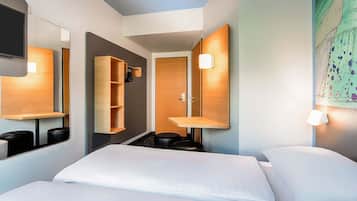 A hotel room with a bed, a wardrobe, a mirror, and a wall-mounted shelf.