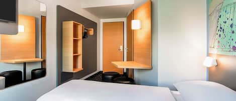 Una habitación de hotel con cama, armario, espejo y estante en la pared.