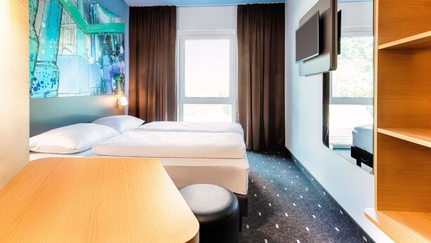A hotel room with two beds, a desk, a TV, and a large window. - B&B Hotel Chemnitz (Chemnitz)