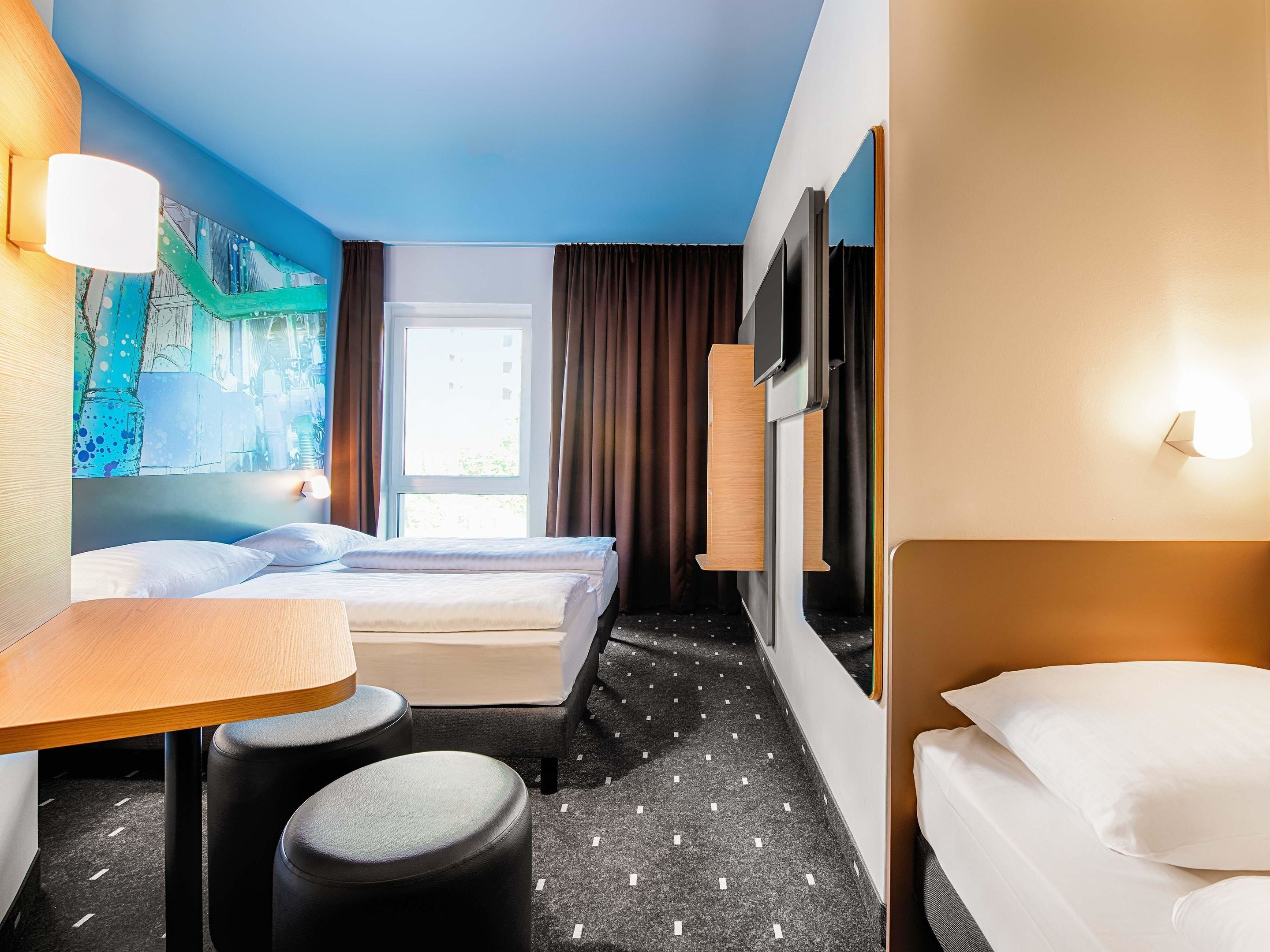 A hotel room with two beds, a desk, and a chair.