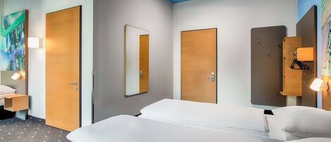 A hotel room with a bed, a nightstand, a mirror, and a wardrobe.