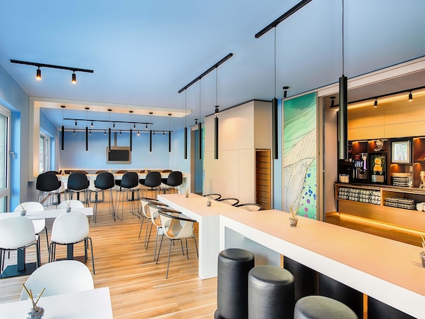 Zona de bar moderna con una barra larga, asientos con taburetes y una máquina de café.