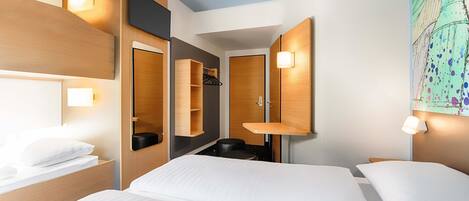 Una habitación de hotel moderna con una cama grande, una mesita de noche, un espejo, un armario y una pequeña zona de estar.