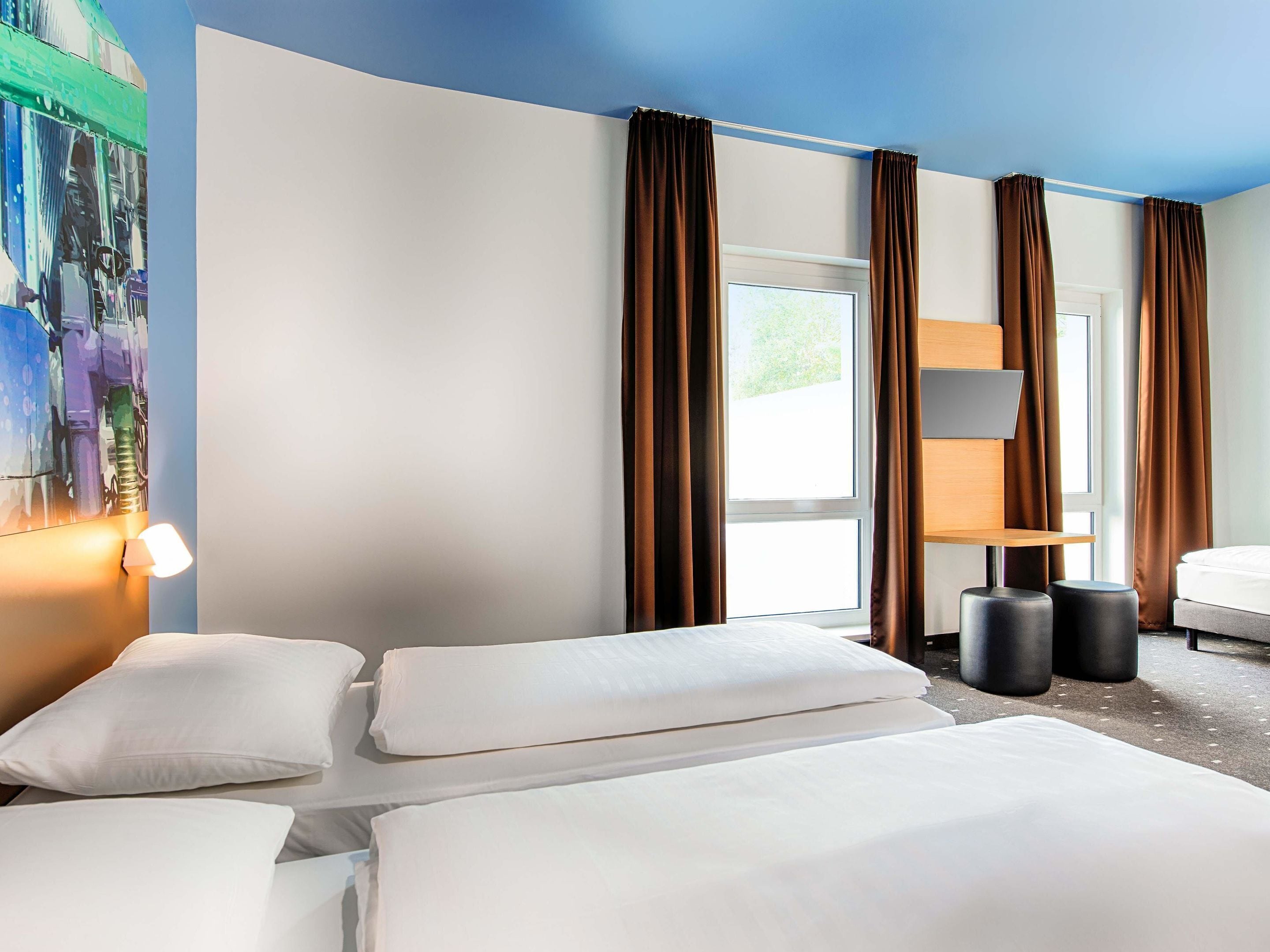 Una habitación de hotel con cama, escritorio, lámpara y un cuadro en la pared.