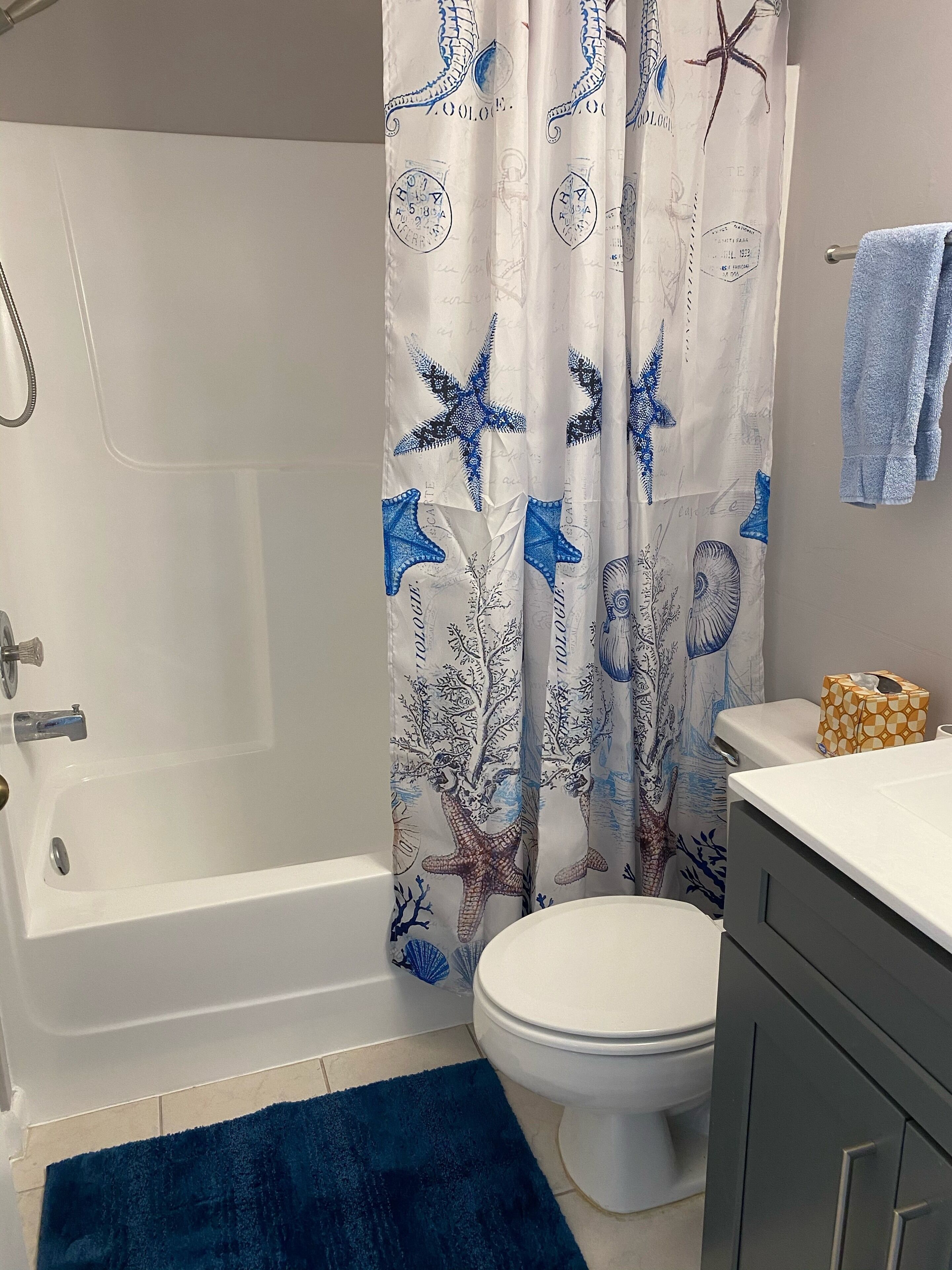 Une salle de bain avec une baignoire, des toilettes et un rideau de douche orné de motifs représentant des étoiles de mer et des coraux.