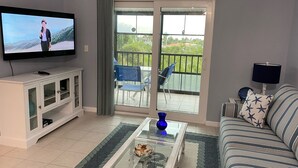 Ein Wohnzimmer mit Fernseher, einer Couch, einem Couchtisch und einem Balkon mit Stühlen.