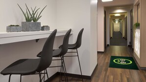 A hotel reception area with a white reception desk, three black bar stools, and potted plants on the counter. - B&B Hotel Düsseldorf-Ratingen (Ratingen)