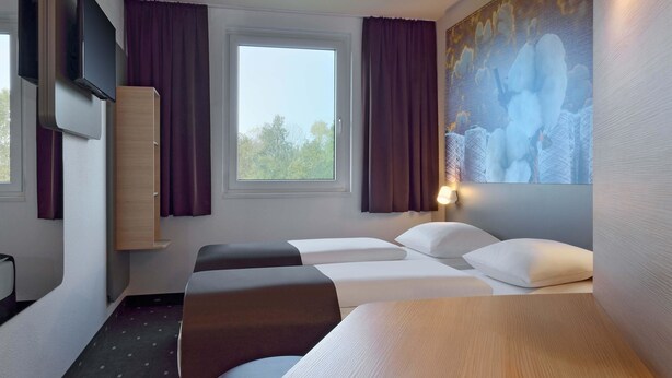 A hotel room with a bed, two bedside tables, a TV mounted on the wall, and a window with curtains. - B&B Hotel Düsseldorf-Ratingen (Ratingen)