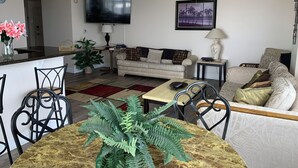 A living room with a sofa, a coffee table, a TV, and a dining area with chairs and a table.