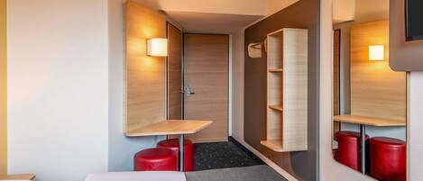 Una habitación de hotel con cama, una mesita, un espejo y un estante con taburetes rojos.