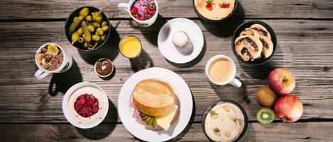 Variedad de alimentos para el desayuno, incluyendo panqueques, un sándwich y frutas frescas como manzanas y kiwi, sobre una mesa de madera.