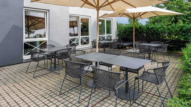 Une terrasse extérieure avec des tables et des chaises, de grands parasols et un bâtiment doté de grandes fenêtres.