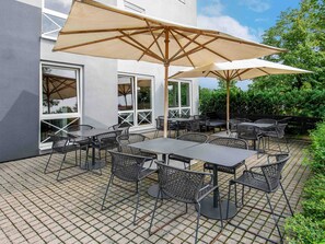 Une terrasse extérieure avec des tables et des chaises, de grands parasols et un bâtiment doté de grandes fenêtres.
