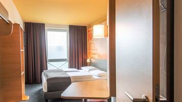 Ein Hotelzimmer mit Bett, kleinem Tisch, Stuhl, Schreibtisch und einem Fenster mit Vorhängen.