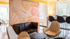 Une chambre d’hôtel moderne, dotée d’un canapé, de fauteuils, d’une petite table et d’une grande fenêtre donnant sur un paysage verdoyant.