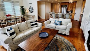 A spacious living room with a wooden coffee table, two white sofas, and a large blue painting on the wall. - Booking NOW for fall! 5 min walk to beach! Wrap @decks. Gulf Views! (Galveston)