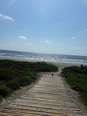 Un sendero de madera que lleva a una playa, con cielo despejado.
