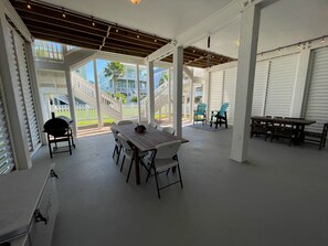 Un porche techado con una mesa y sillas de madera, una parrilla y vistas a una zona residencial con valla blanca y casas.