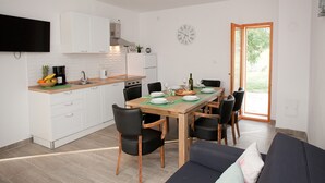 A modern kitchen with white cabinets, a wooden dining table, and black chairs. There is a flat-screen TV mounted above the counter, and a clock on the wall. - Villa Natura (Benkovac)