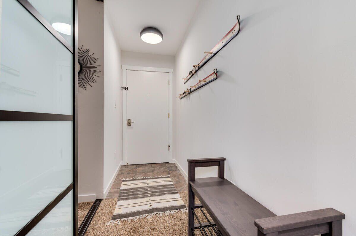 A hallway with a white door, a bench, a ski rack, and a sunburst decoration on the wall.