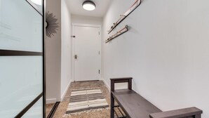 Un couloir avec une porte blanche, un banc, un porte-skis et une décoration en forme de soleil sur le mur.